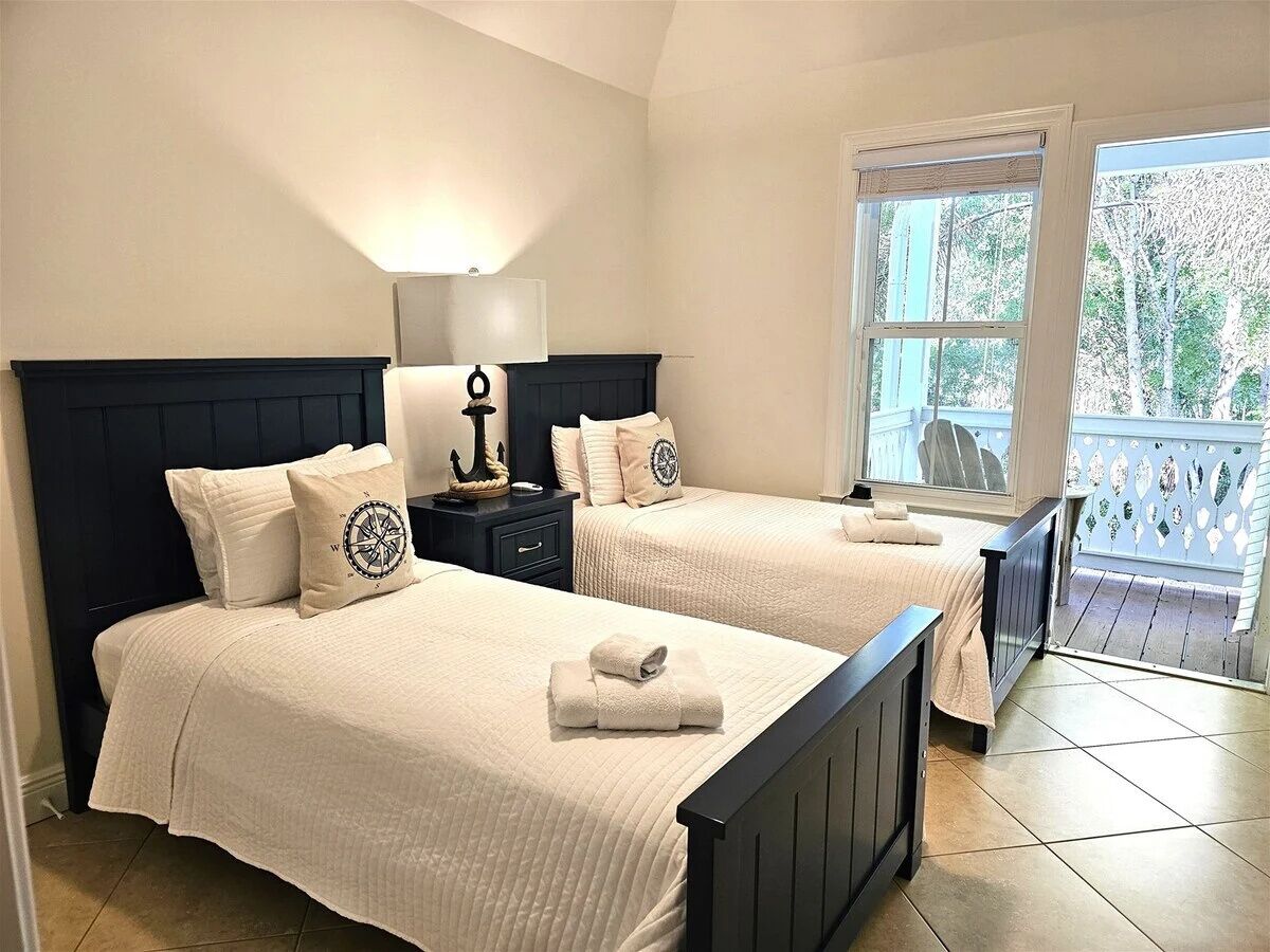 A bedroom with two beds, a nightstand, a lamp, and a window with a view of trees.