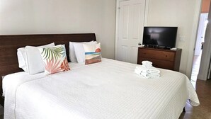 Ein Hotelzimmer mit einem großen Bett, einem Fernseher auf einer Holzkommode und einer Tür rechts.