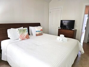 Ein Hotelzimmer mit einem großen Bett, einem Fernseher auf einer Holzkommode und einer Tür rechts.