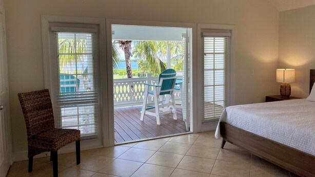 Ein Hotelzimmer mit einem Bett, einem Sessel, einem Tisch und Blick auf einen Pool sowie Palmen durch eine Schiebetür.