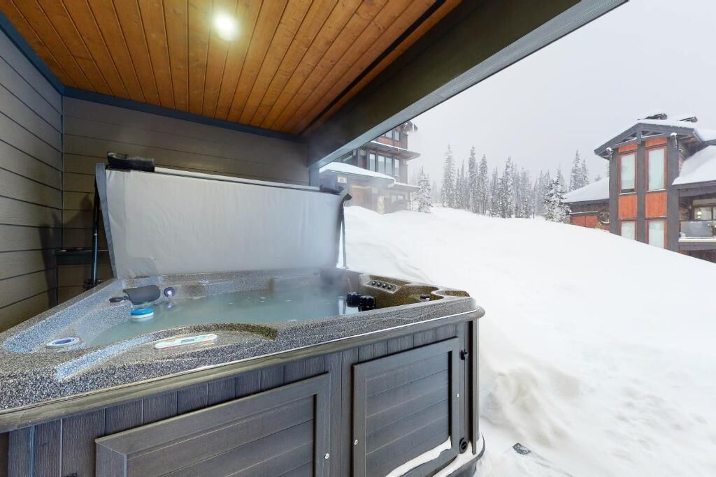 A hot tub with a wooden ceiling and a view of snow-covered buildings.