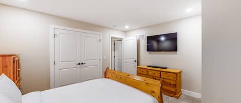 A bedroom with a bed, wooden dresser, wardrobe, and a TV on the wall.