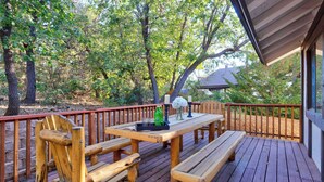 Eine Holzterrasse mit Tisch und Bänken, umgeben von Bäumen.