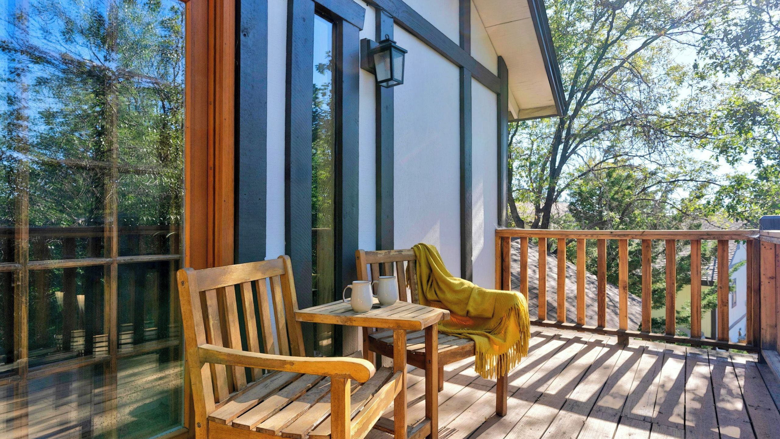 A wooden deck with a bench and table, a lantern, and a view of trees.