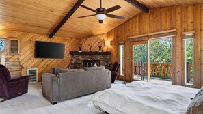 A spacious room with a large bed, a sofa, a fireplace, and a television. - Pinewood Perch by Avantstay Layered Decks + Grill + Multiple Living Spaces Slopes + Lake Nearby (Big Bear City)