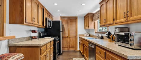 A compact kitchen with wooden cabinets, a black refrigerator, a microwave, a toaster, and a dishwasher.