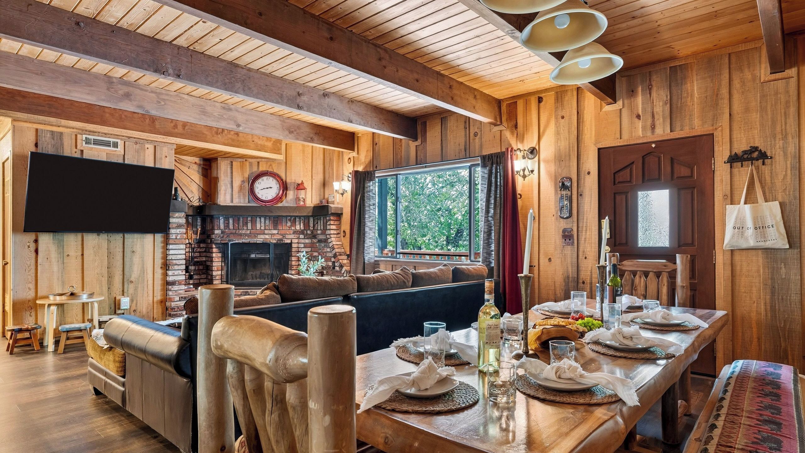 A wooden interior with a fireplace, a sofa, a dining table set for four, and a large window.