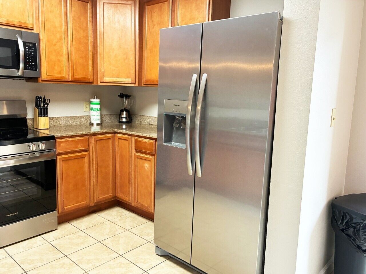 A kitchen with wooden cabinets, stainless steel appliances including a refrigerator and microwave, and a gas stove.