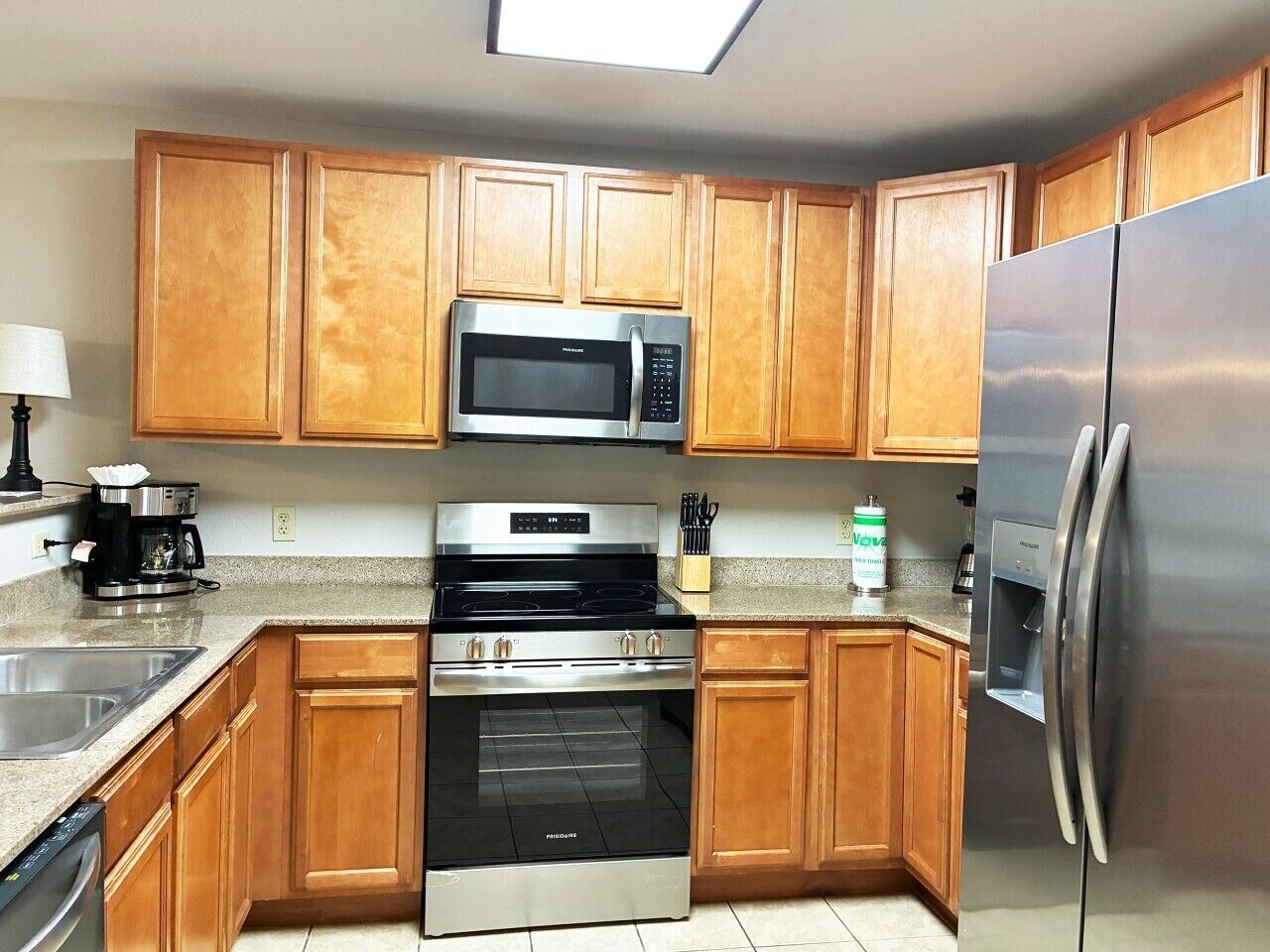 A kitchen with wooden cabinets, a stainless steel microwave, a stove, a refrigerator, and a water dispenser.