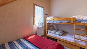 Une chambre avec un lit superposé, une fenêtre, des murs en bois et une couverture rouge.