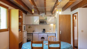 A compact kitchen with a microwave, coffee maker, and washing machine. There is a dining table with chairs and a wooden ceiling.