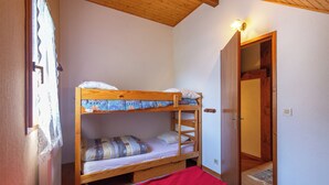 A bunk bed room with a wooden ceiling, a door, and a window with curtains.