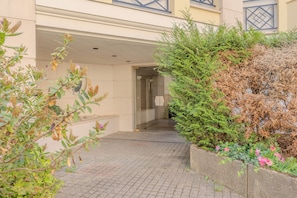A paved entrance to a building with a glass door, surrounded by greenery and a small flower bed. - Le Versaillais - Petfriendly - Wifi (Versailles)