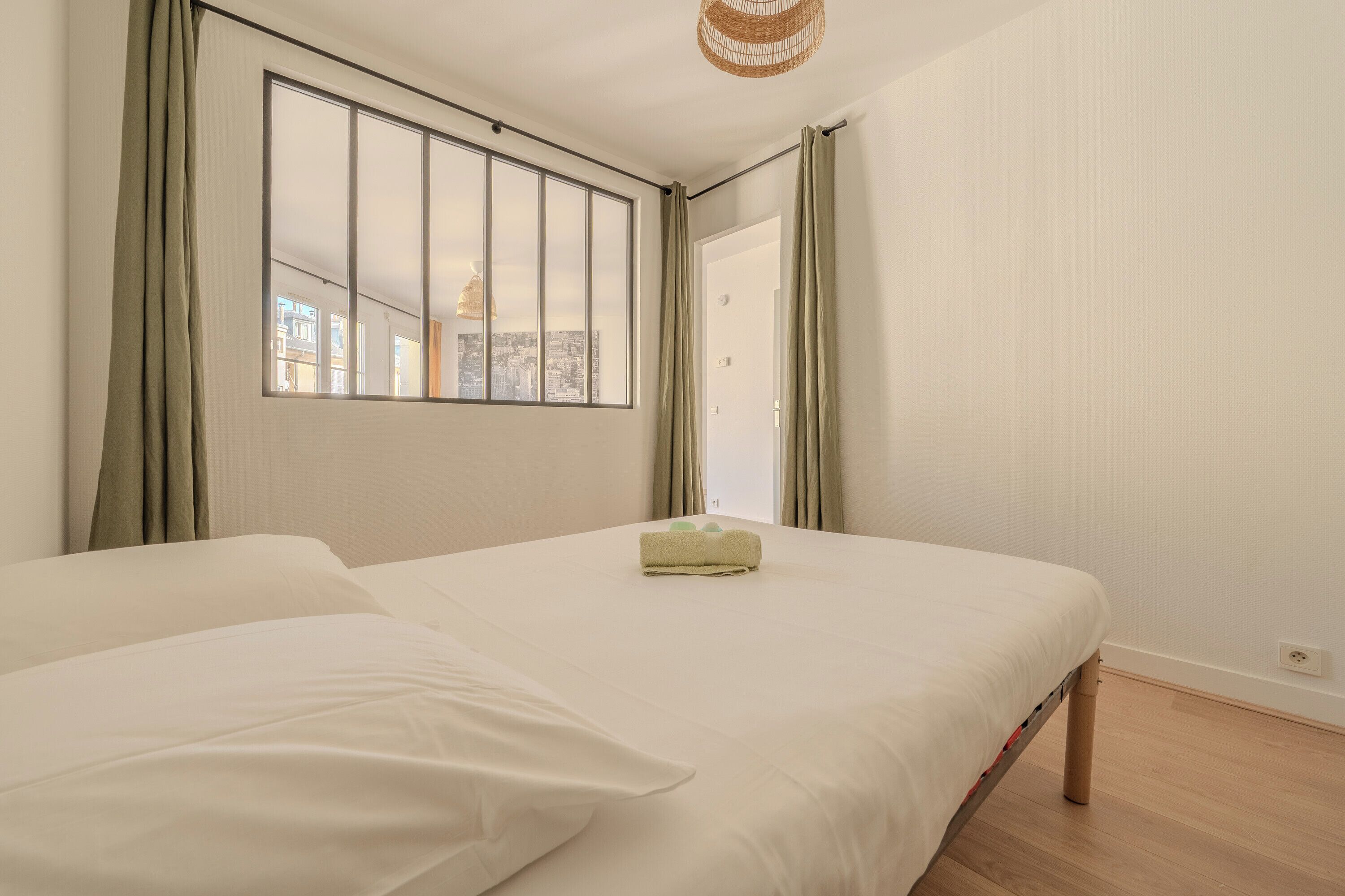 A bedroom with a large window, a bed, and a view of the cityscape.
