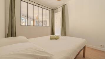 A bedroom with a large window, a bed, and a view of the cityscape.