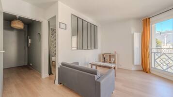 A modern living room with a sofa, a dining table, and a large window with curtains.