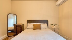 Ein Schlafzimmer mit einem Bett, einer Kommode, einem Spiegel und einem kleinen Tisch mit Pflanze.
