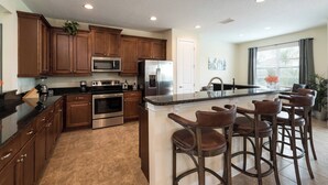 A kitchen with wooden cabinets, stainless steel appliances, a central island with bar stools, and a large window. - Disney Dreams Luxury Home With Private Water Park (Kissimmee)