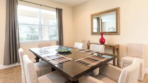 A dining room with a glass table, beige chairs, a red vase, and a mirror on the wall. - Disney Dreams Luxury Home With Private Water Park (Kissimmee)