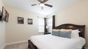 A bedroom with a bed, ceiling fan, wall art, and a window with curtains. - Disney Dreams Luxury Home With Private Water Park (Kissimmee)