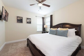 Ein Schlafzimmer mit Bett, Deckenventilator, Wandbildern und einem Fenster mit Vorhängen.