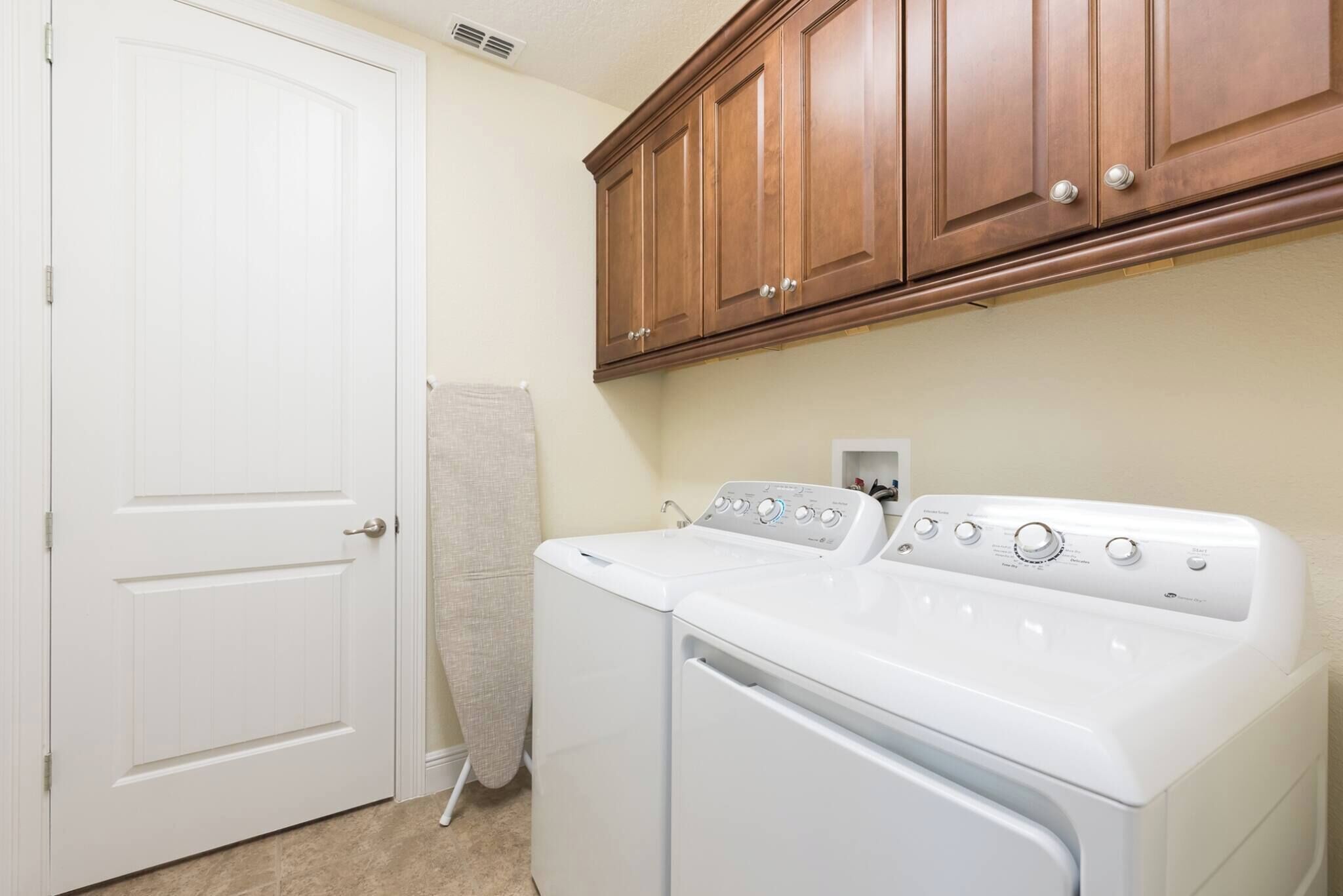 Une buanderie avec une porte blanche, des armoires en bois, ainsi qu’un lave-linge et un sèche-linge à chargement frontal.