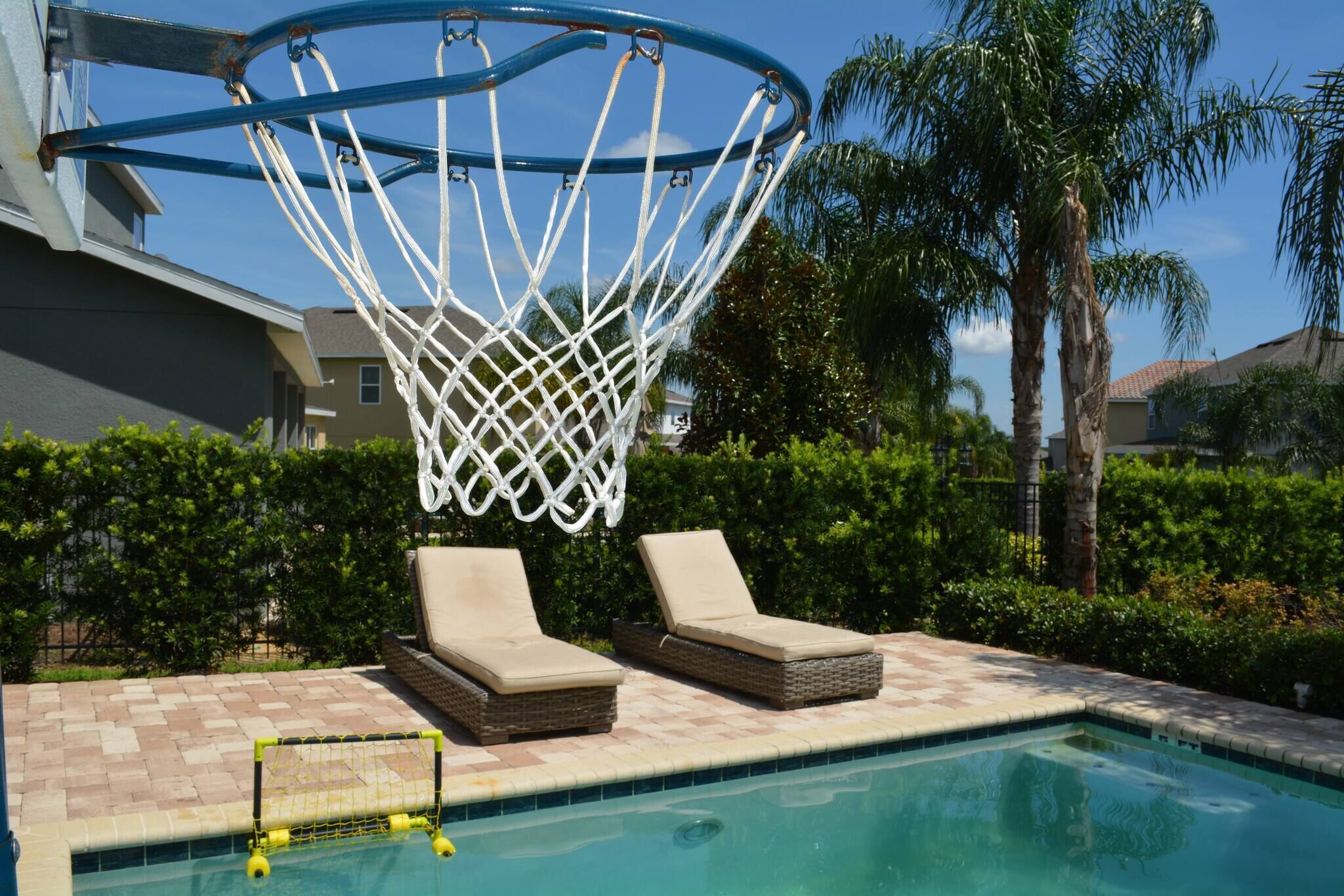 Une piscine équipée d’un panier de basketball et de chaises longues.