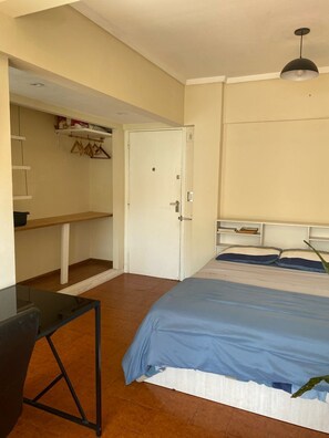 A bedroom with a bed, a desk, a chair, a wardrobe, and a hanging light fixture. - Studio apartment in the Guemes-Aldrey area (Mar del Plata)
