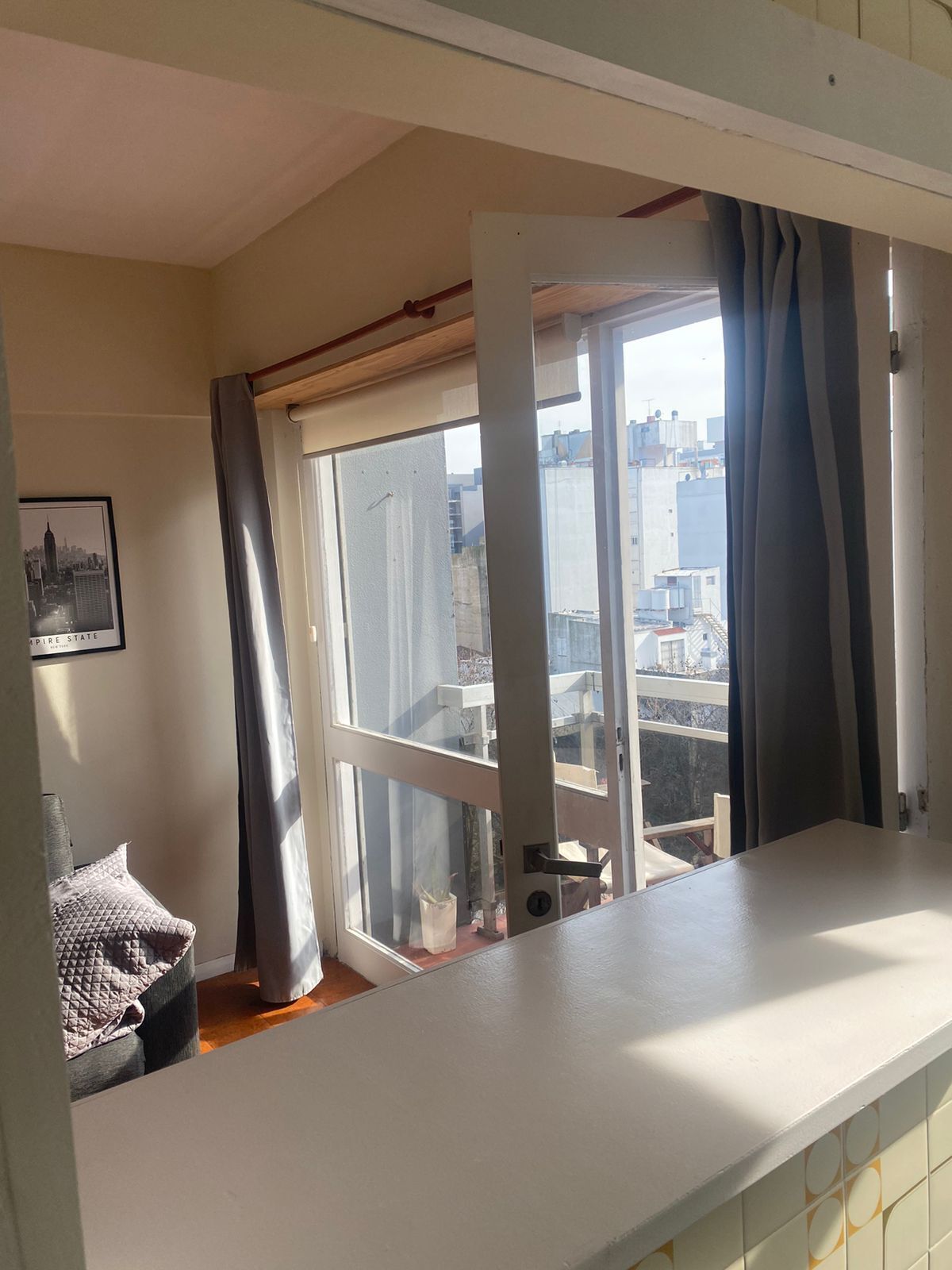 Una habitación con un ventanal, vistas a edificios y un cuadro en la pared.
