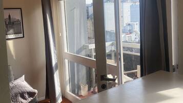 Una habitación con un ventanal, vistas a edificios y un cuadro en la pared.