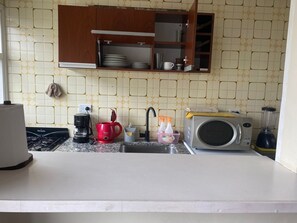 A kitchen with a gas stove, coffee maker, red mug, microwave, and a sink. - Studio apartment in the Guemes-Aldrey area (Mar del Plata)