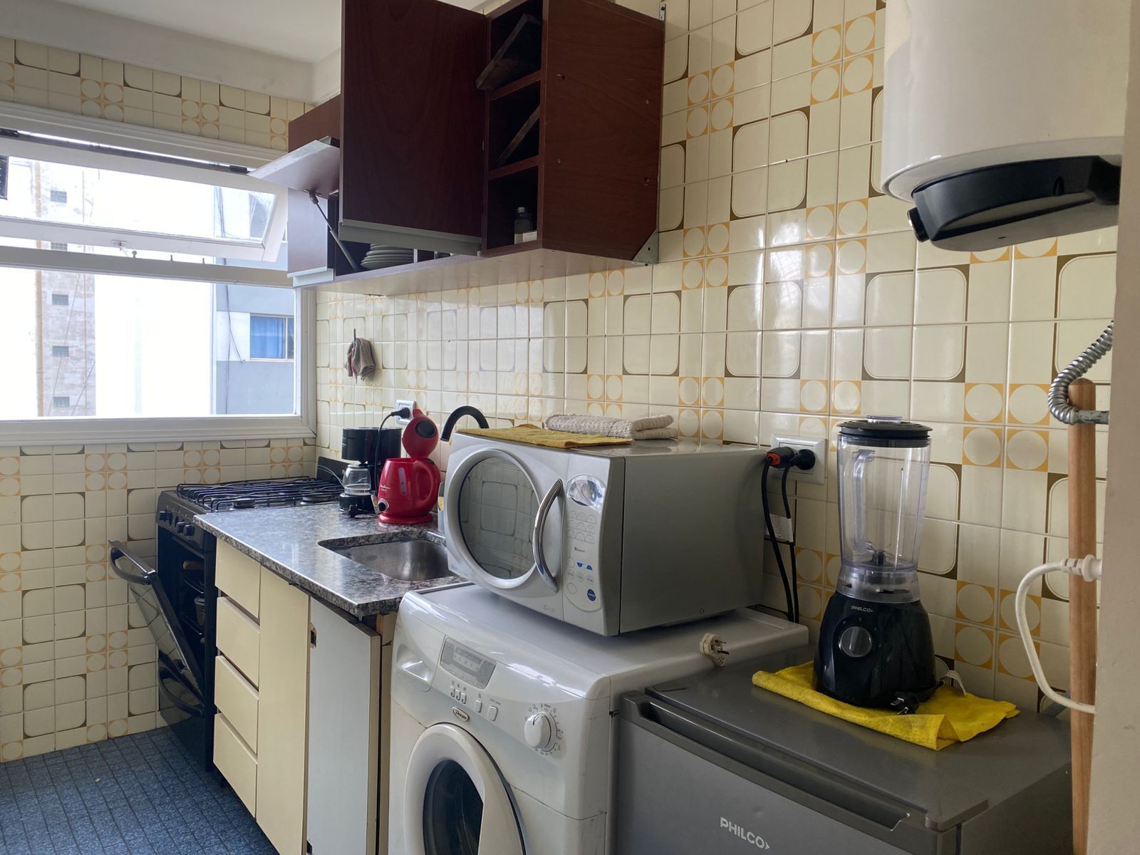 Une cuisine compacte équipée d’un lave-linge, d’une machine à café et d’un mixeur, le tout posé sur le plan de travail.