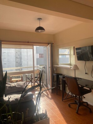 A room with a desk, chair, TV, and large windows.