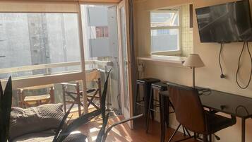 Una habitación con escritorio, silla, televisor y un ventanal grande.