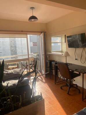 A room with a desk, chair, TV, and a large window. - Studio apartment in the Guemes-Aldrey area (Mar del Plata)