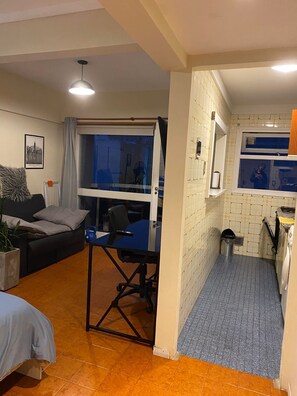 A compact living space with a bed, a desk, a chair, a small kitchenette, and a window. - Studio apartment in the Guemes-Aldrey area (Mar del Plata)
