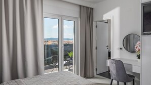Ett modernt hotellrum med en säng, ett skrivbord, en stol, en rund spegel och en balkong med utsikt.