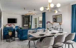 A modern dining area with a white table set for four, blue sofas, and a chandelier. - Lovely home in Zadar with sauna (Zadar)