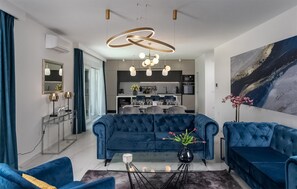 A modern living room with a blue sofa set, a glass coffee table, and a unique circular light fixture. - Lovely home in Zadar with sauna (Zadar)