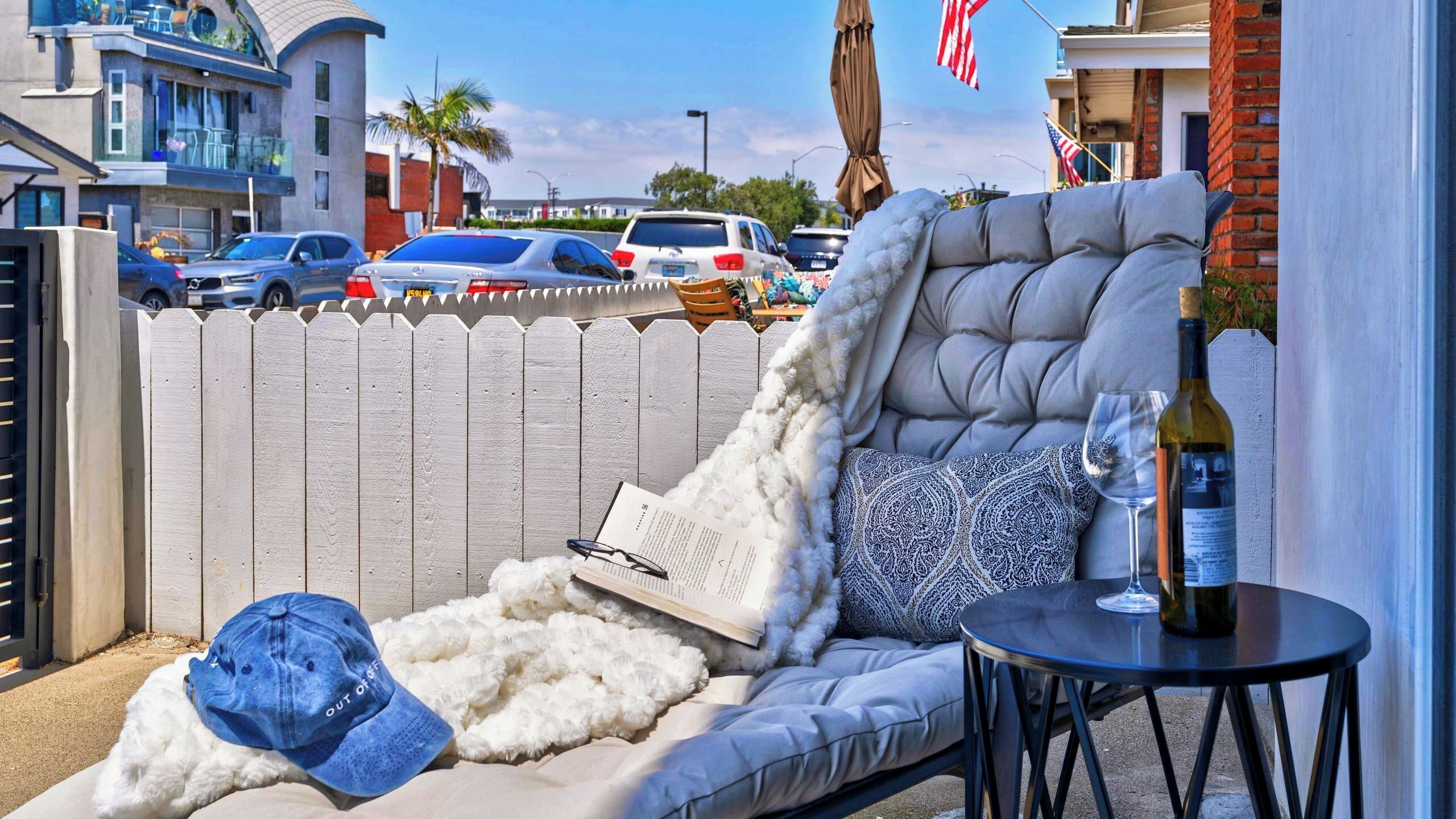 A balcony with a cushioned seating area, a small table with a bottle and glass, and a book.