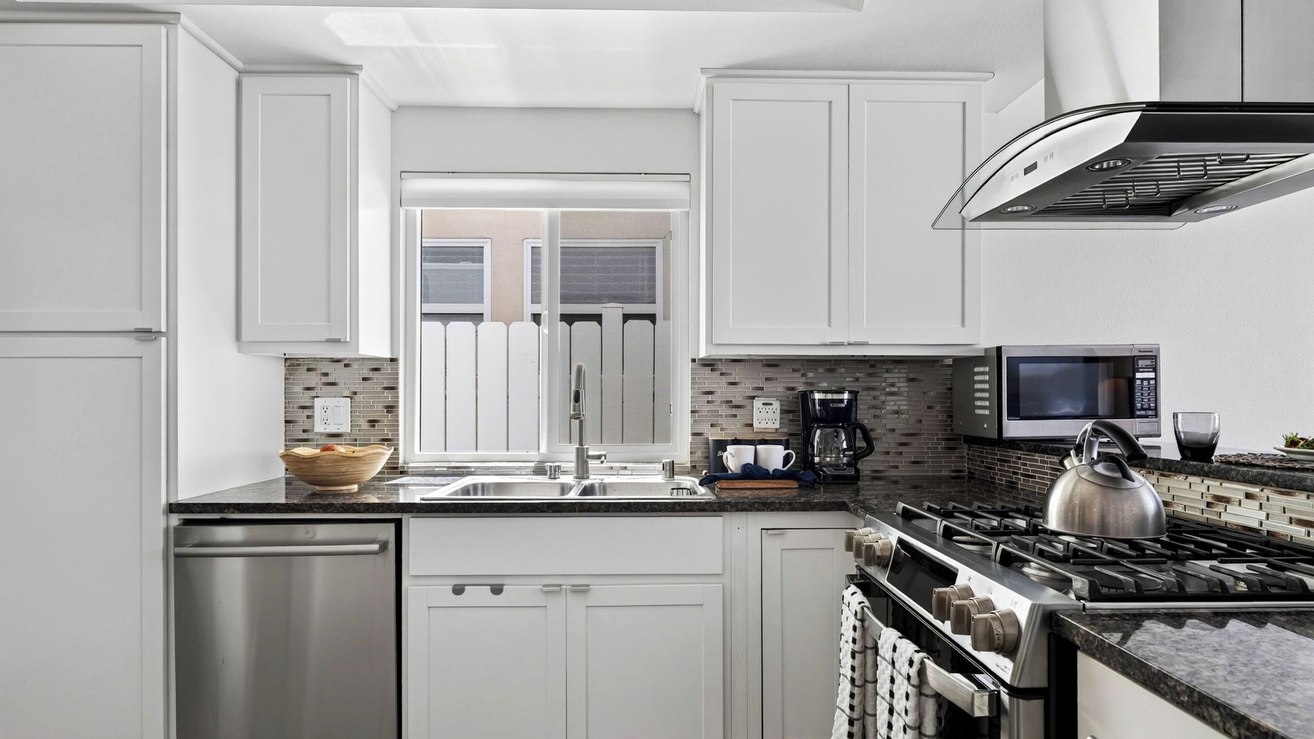 A modern kitchen with white cabinetry, a stainless steel dishwasher, a gas stove, a microwave, and a coffee maker.