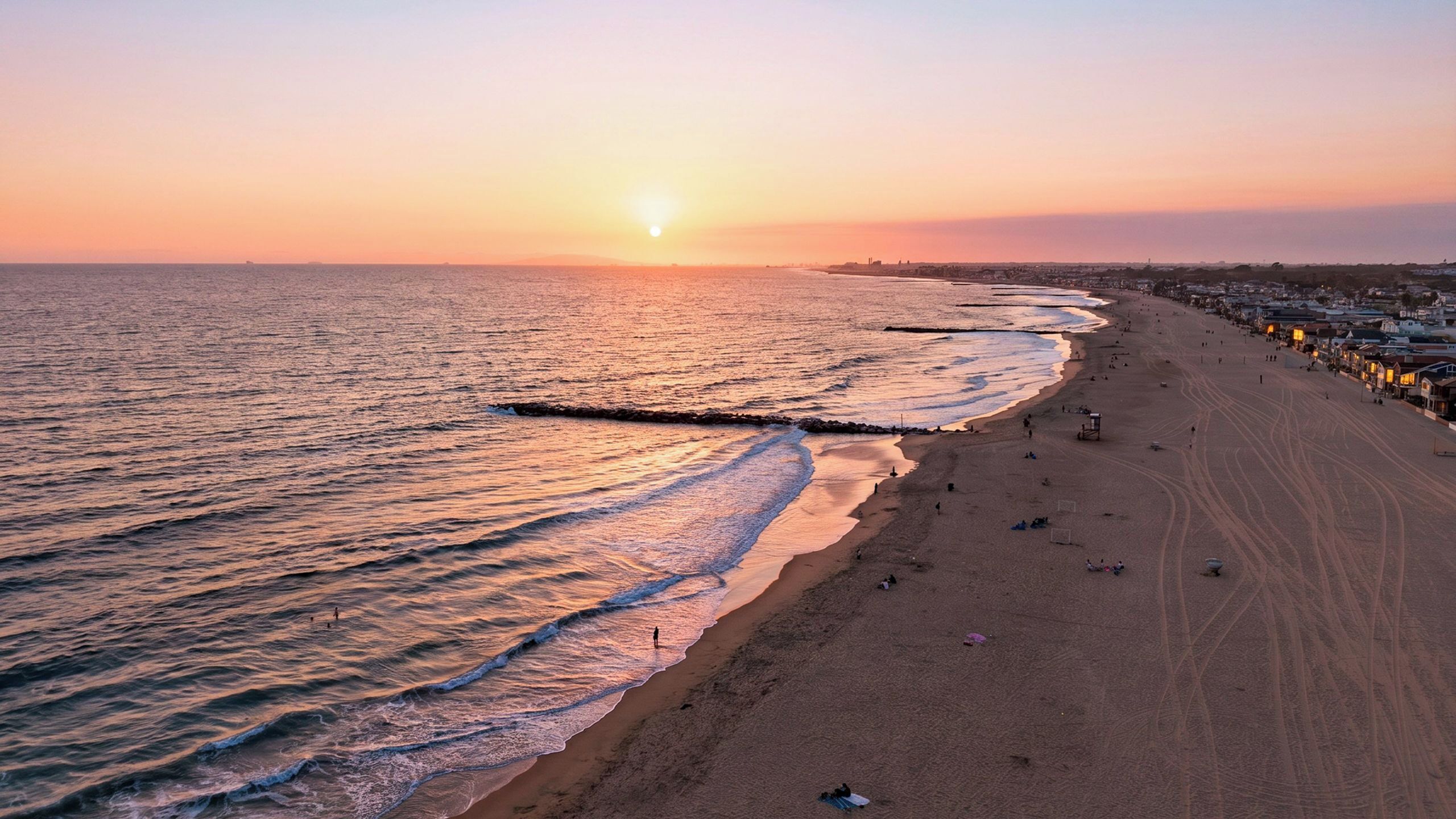 A beach with a pier extending into the water, a clear sky, and a sunset.