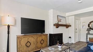 A living room with a flat-screen TV, a fireplace, a wooden cabinet, and a coffee table with books and a bowl.