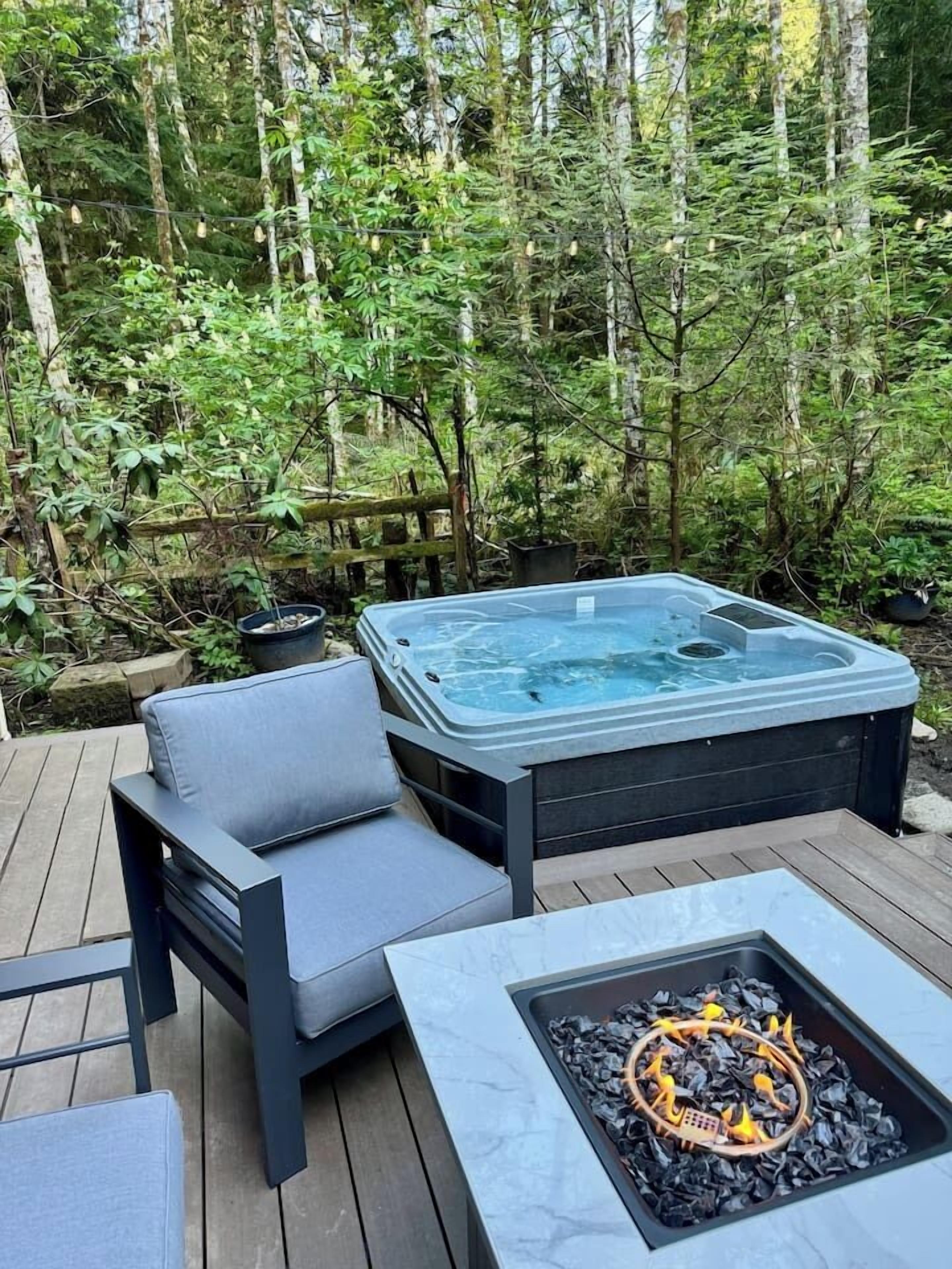 A hot tub surrounded by a wooden deck, with a fire pit in the foreground.