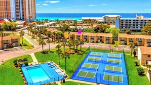 Um hotel com várias quadras de tênis, piscina e vista para o oceano.