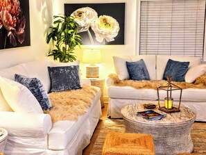 Ein Wohnzimmer mit zwei weißen Sofas, einem runden Couchtisch, einer Stehlampe und einem großen Blumenbild an der Wand.