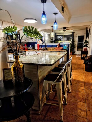 Una cocina con una isla central, taburetes de bar, iluminación colgante y una planta en maceta.