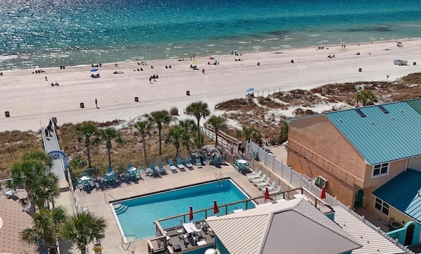 Blick auf einen Strand mit Swimmingpool, Liegestühlen und einem Gebäude mit blauem Dach.