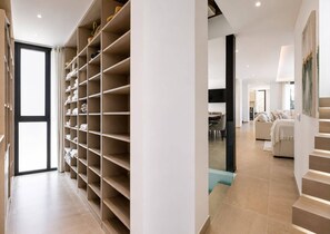 A modern interior with a large open shelving unit, a staircase, and a living area with a sofa and a dining table. - The Solstice Estate – Private Pool Retreat for Families & Groups (Marbella)