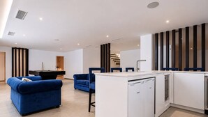 A modern kitchen with a central island, blue sofas, and a staircase in the background. - The Solstice Estate – Private Pool Retreat for Families & Groups (Marbella)